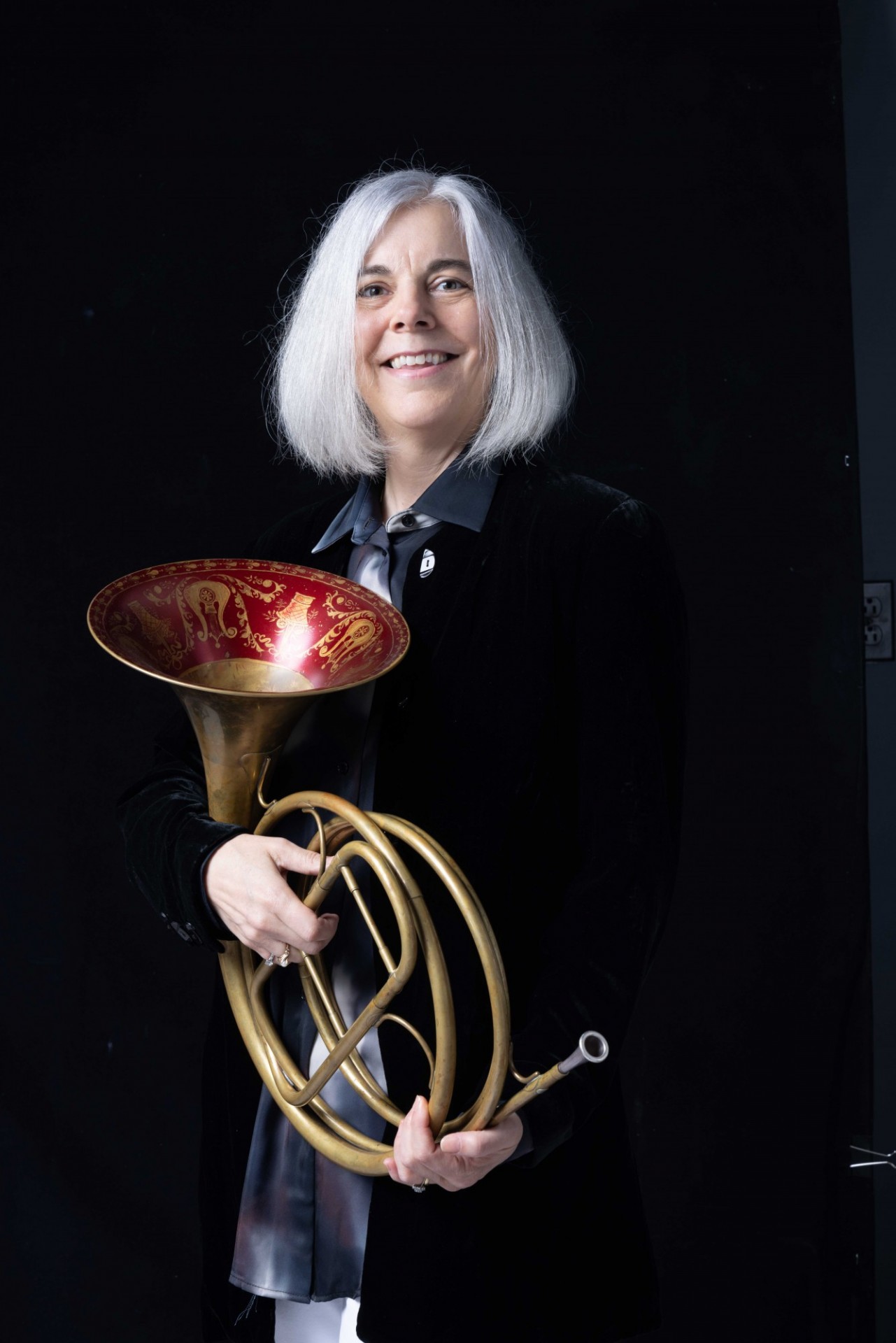 Dr. Strauchen-Scherer holding a French horn. The inside of the bell is embossed with a red design. She is on a black background.