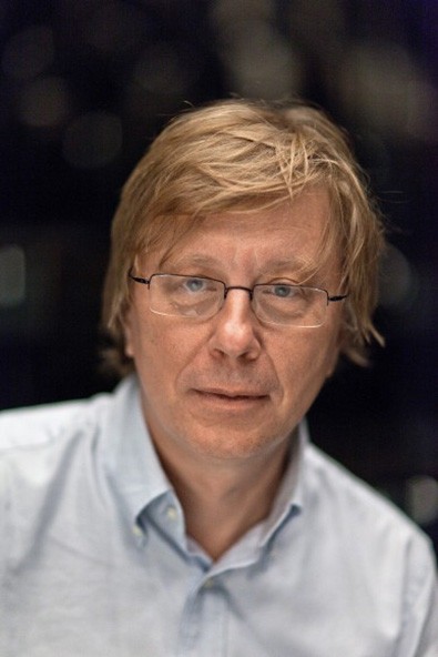 Georg Haas in a light blue shirt in front of a dark background.