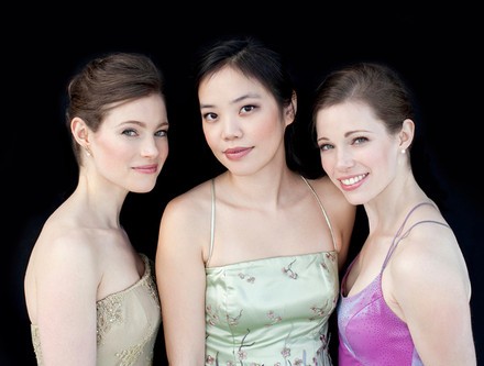 Claremont Trio. They are standing in front of a black background with pastel tops.
