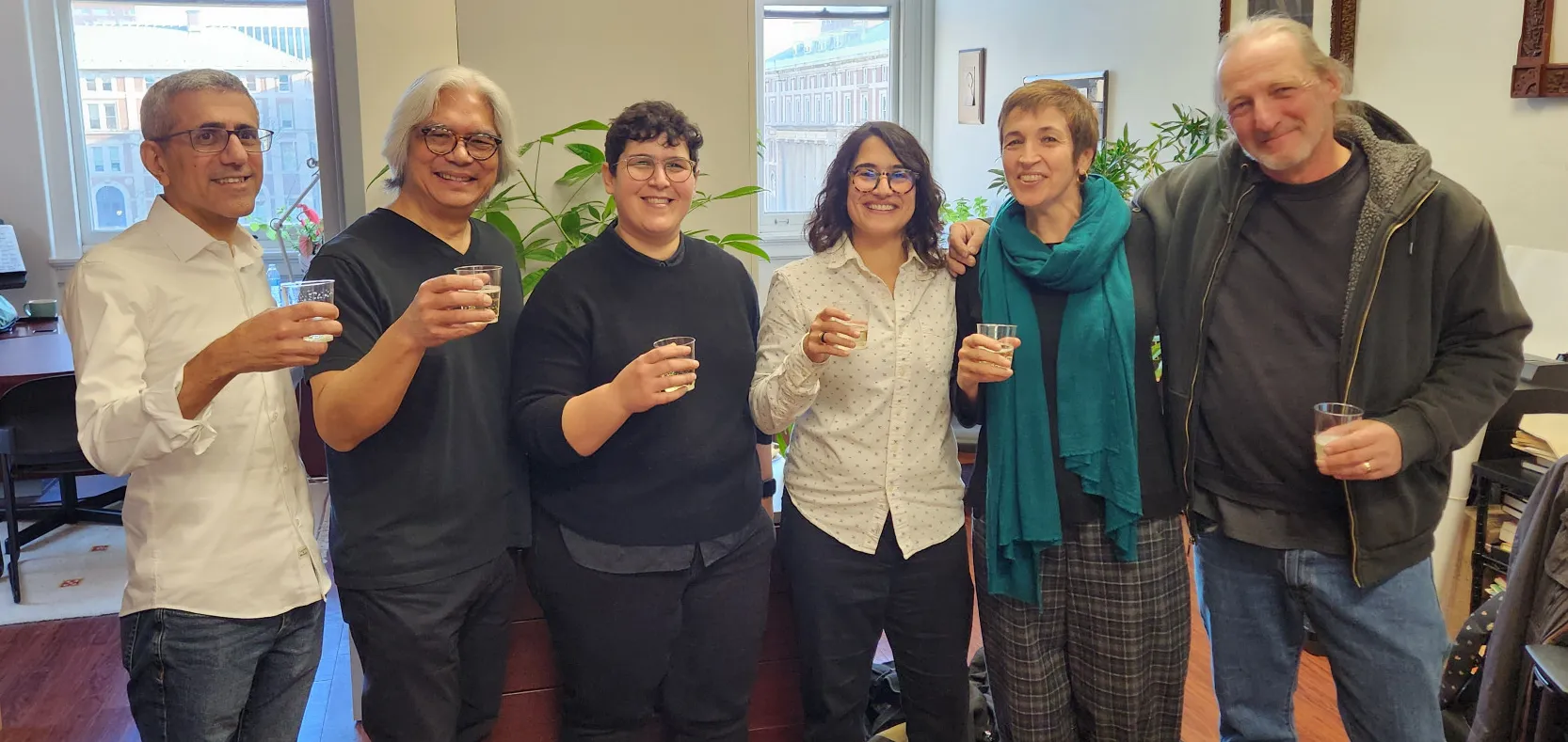 Paola with her committee in the Music Department office. They are all holding glasses with bubbly liquid inside.