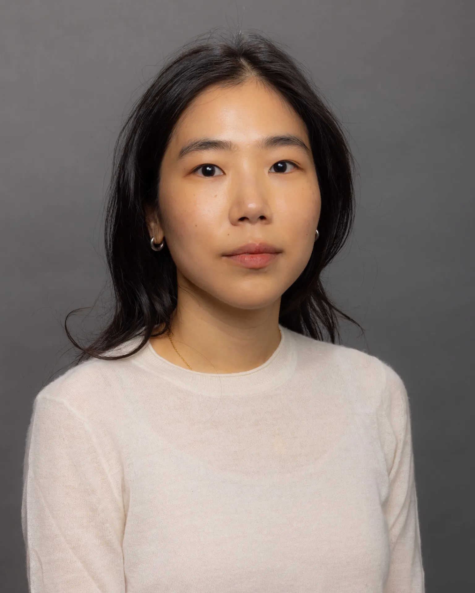 Laurie Lee sits facing the camera. She is wearing an off-white top against a dark gray background.