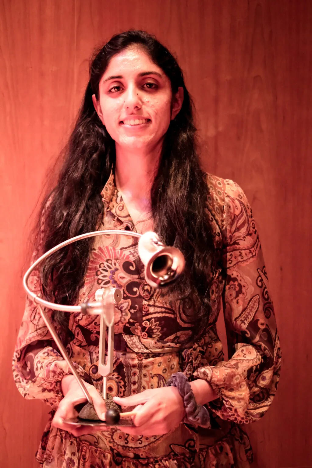 Zara Ali in a red and orange patterned dress holds the Gaudeamus Award, a spiral of metal that allows one to hear one's voice as others hear it.