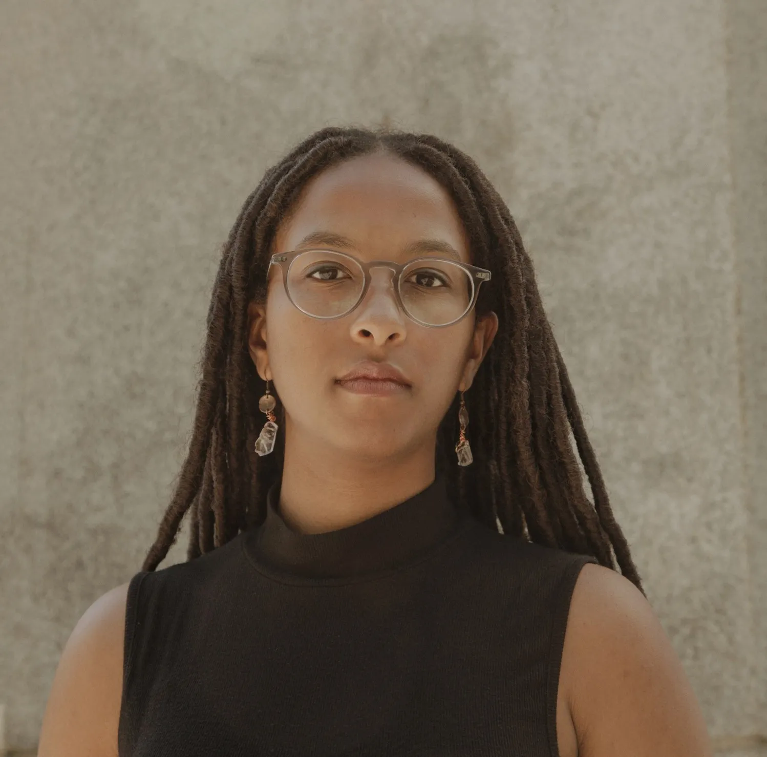 Corie Rose Soumah looks at the camera in a black top against a concrete background.