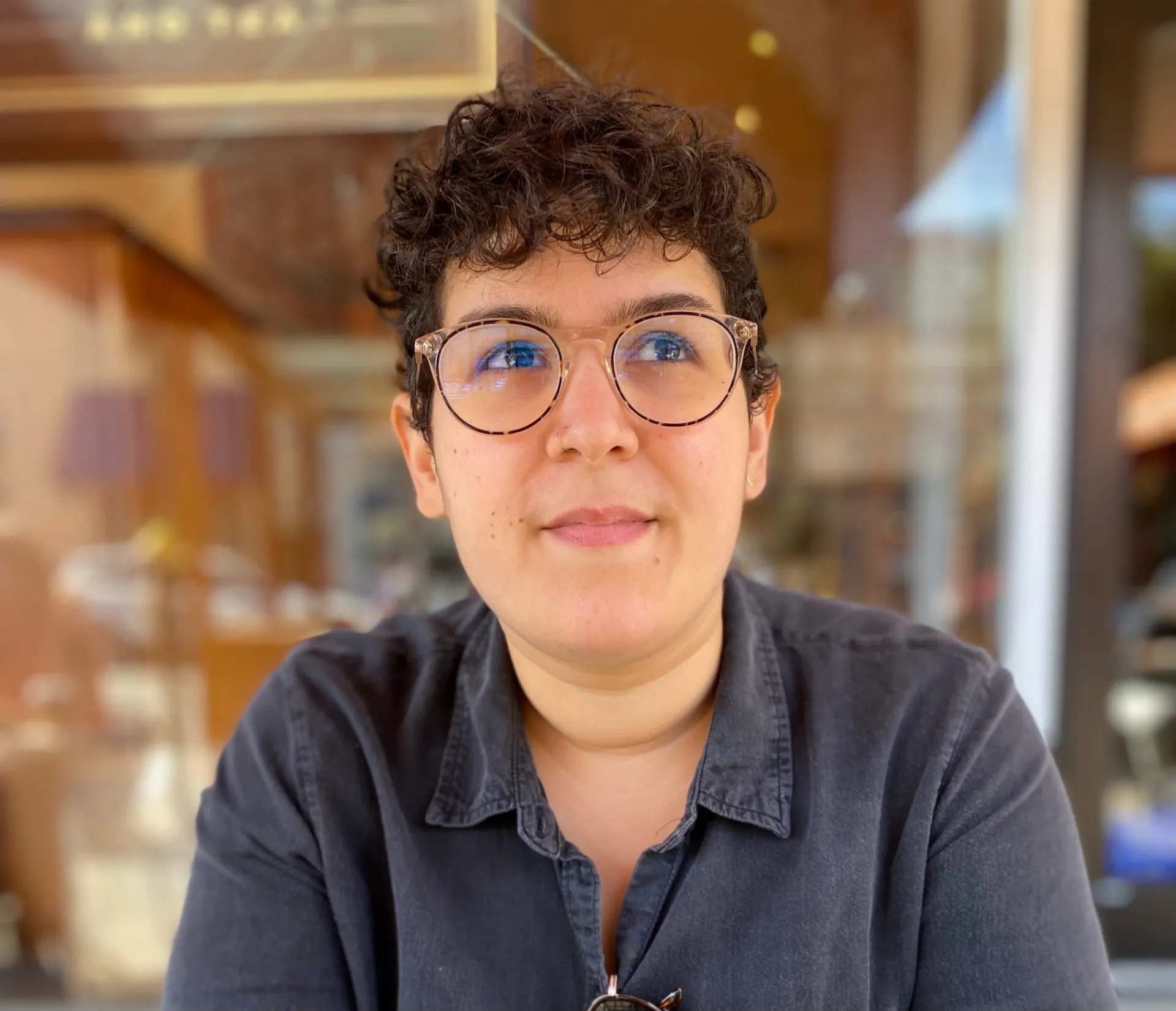 Nour El Rayes looks up and to the right with a slight smile. She is wearing a dusky blue shirt.