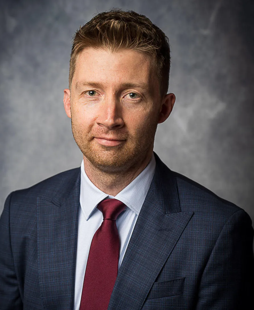 Galen DeGraf in blue suit and a red tie, and he's in front of a blue background. He's slightly smiling at the camera.