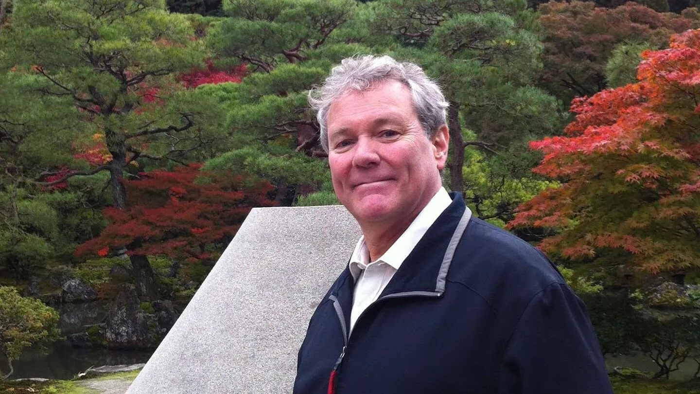 Brad Garton smiling in front of red and green foliage.