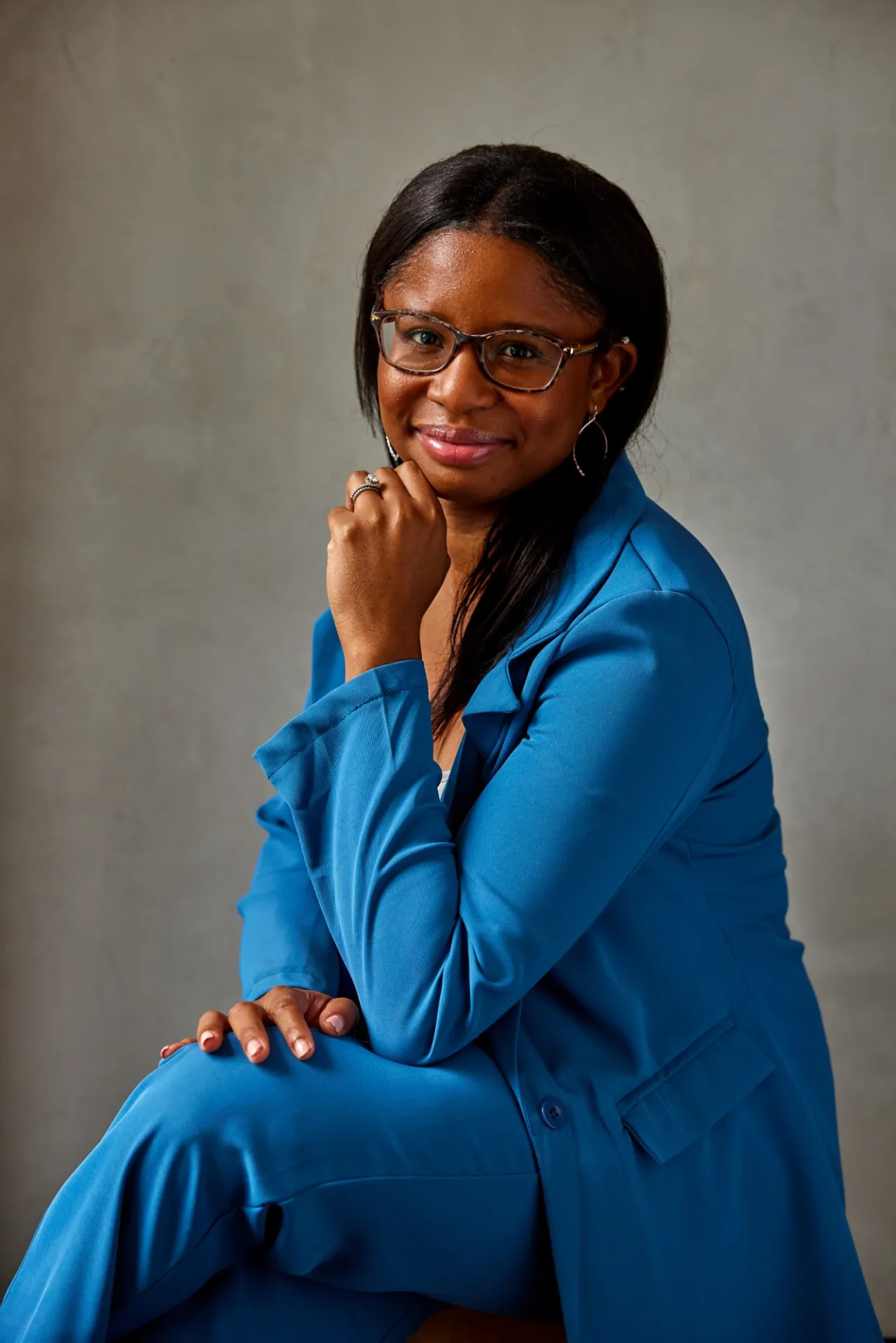Jasmine Henry in a blue suit in front of a beige background.