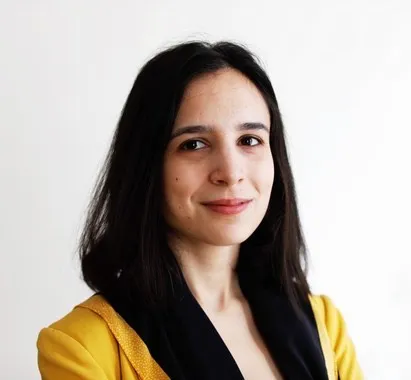 Headshot of Velia Ivanova. She is in front of a white background and has long dark hair and a yellow shirt.