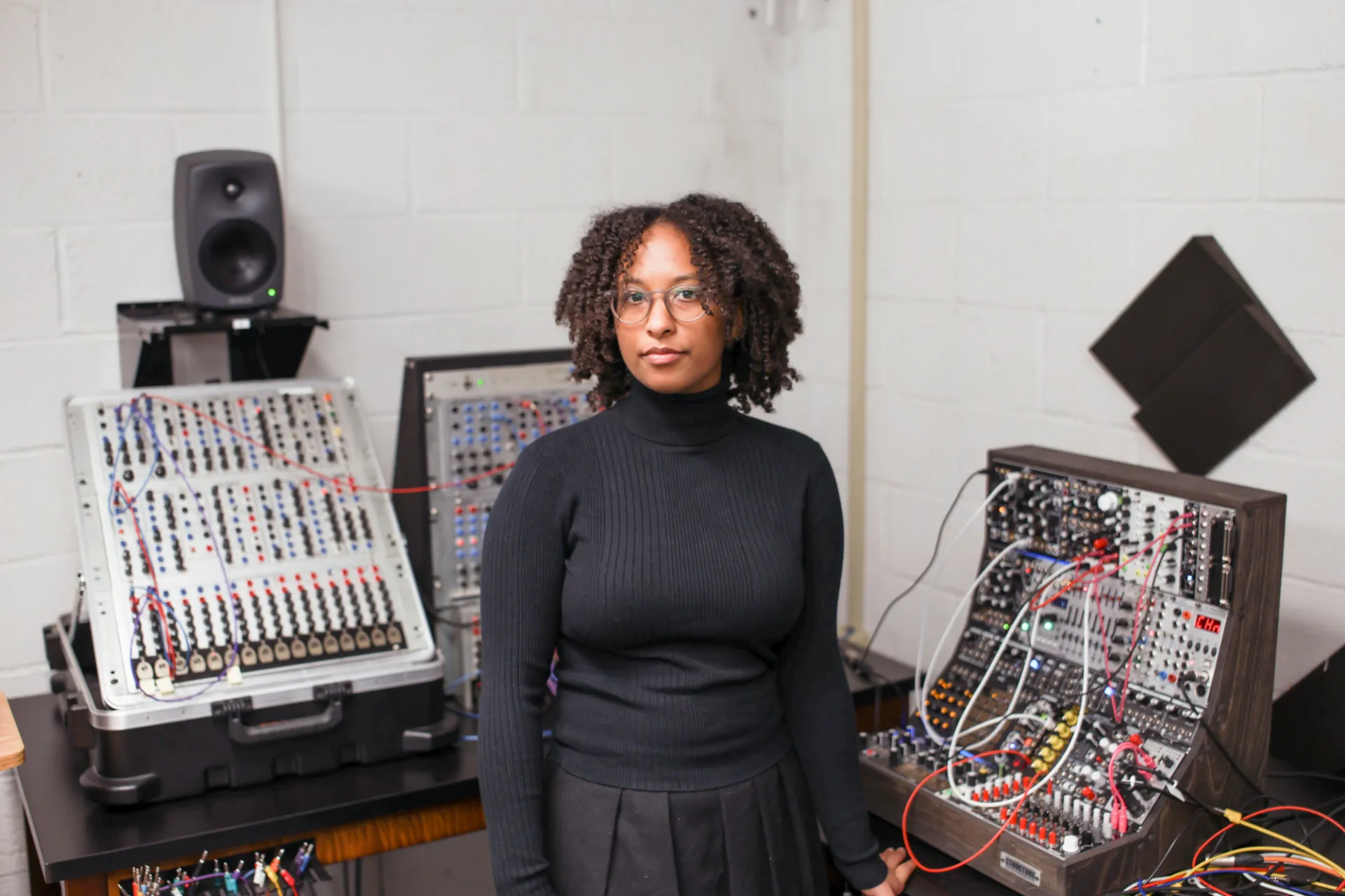 Corie Rose Soumah stands in front of wires, cables, and interfaces in the Department of Music.