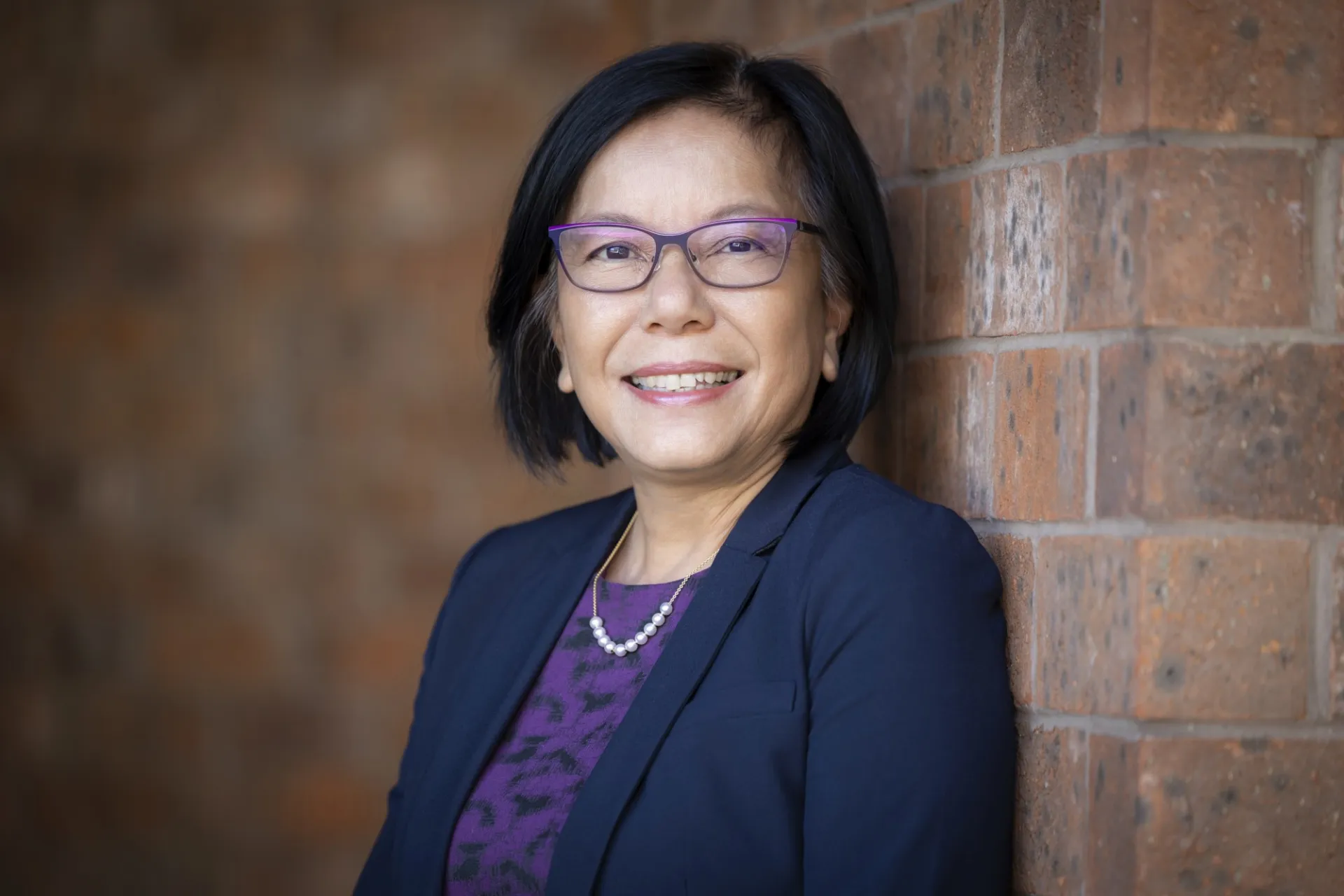 Nancy Rao in a blue suit smiling at the camera. Her back is to a brick wall.