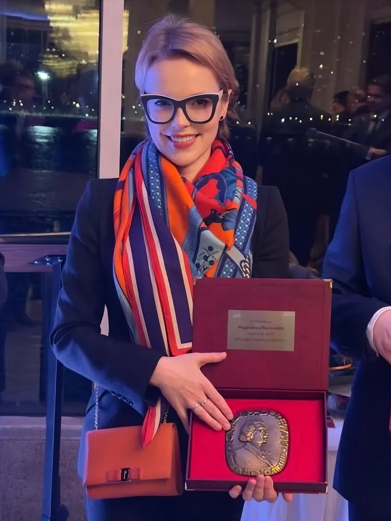 Magdalena Stern-Baczewska in a navy suit and a red, blue, white and orange scarf as she holds the award in her hands.