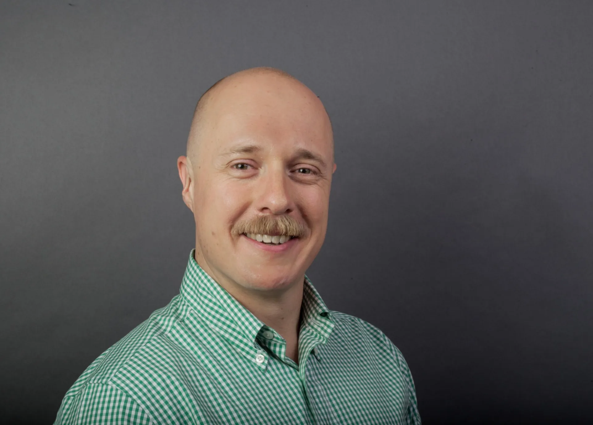 Marc Hannaford dressed in a green and white checkered button down, in front of a gray background.