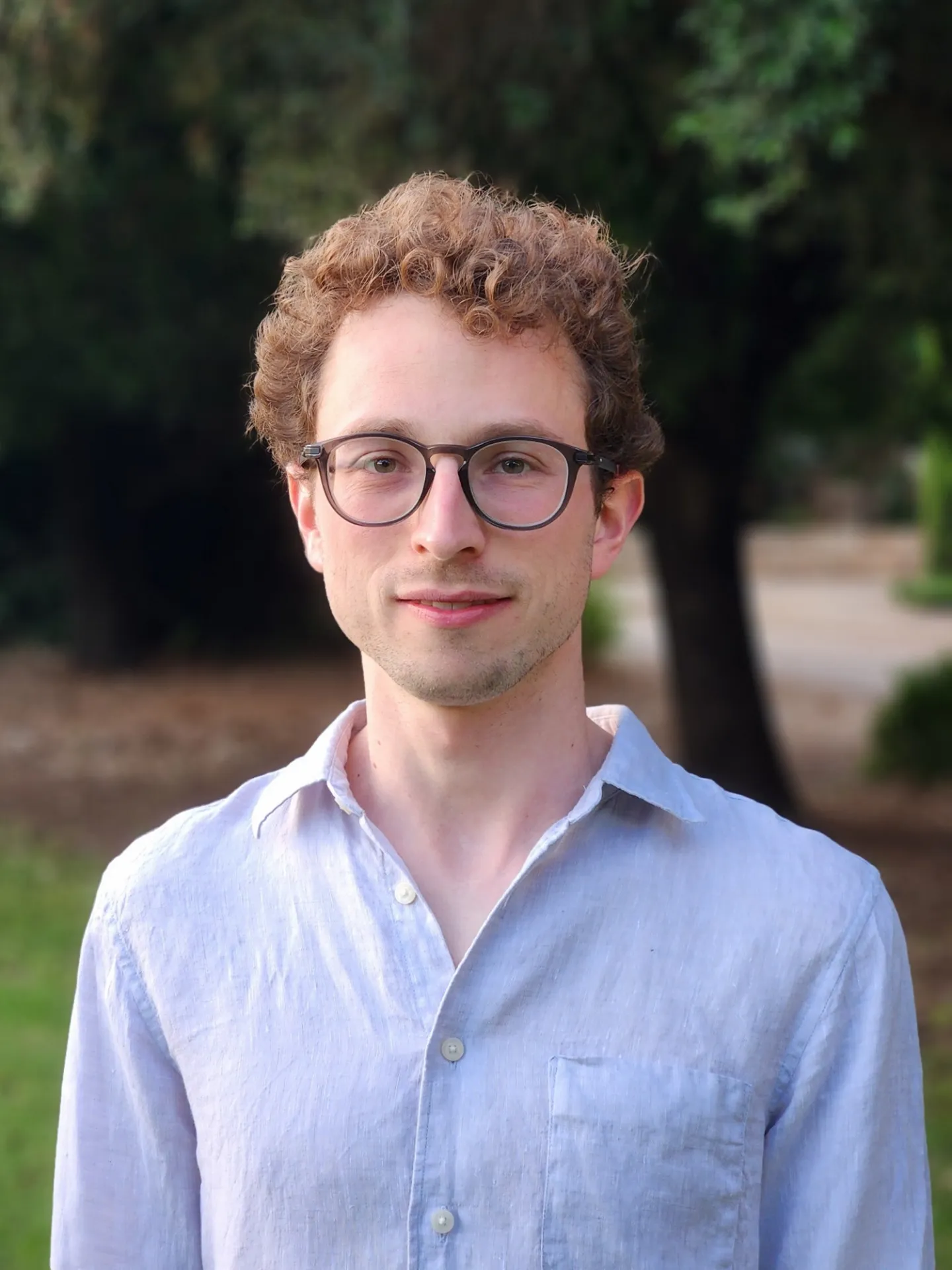 Omer Barash headshot. He's in a white button-down in front of a background of trees.