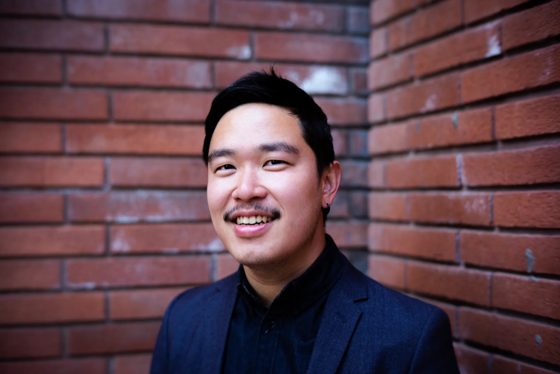 Dr. Wangpaiboonkit in a blue suit in front of a dark red brick background.