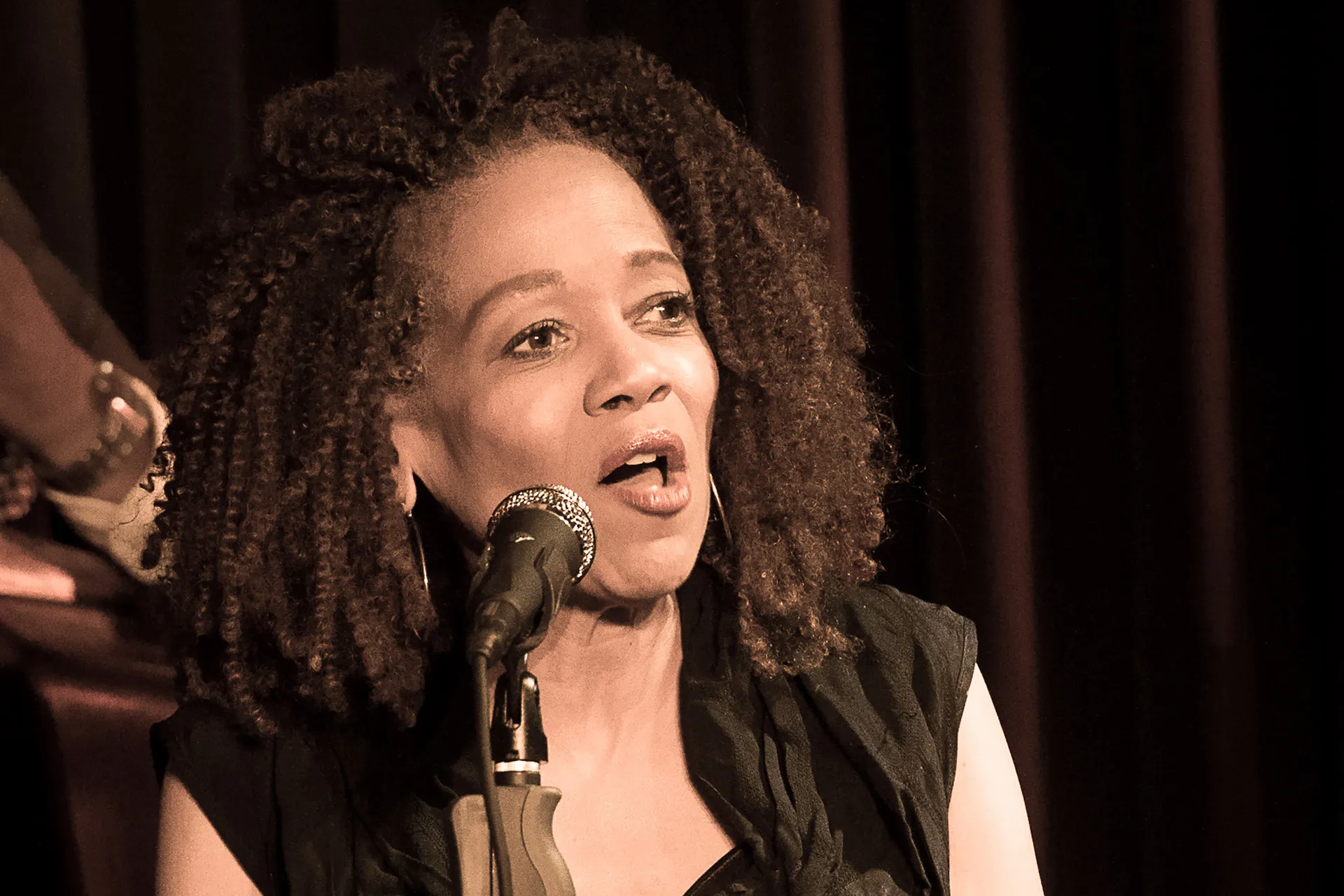 Paula West wears a black top and looks to her left, singing.