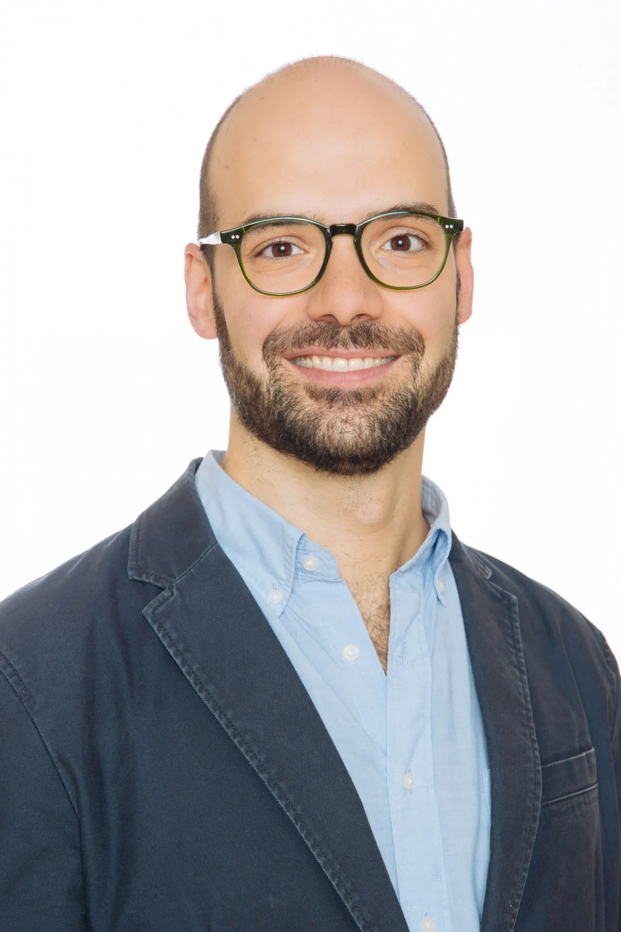 Milella in a dark jacket and light blue shirt, smiling against a white background. He has a bald head and dark glasses.