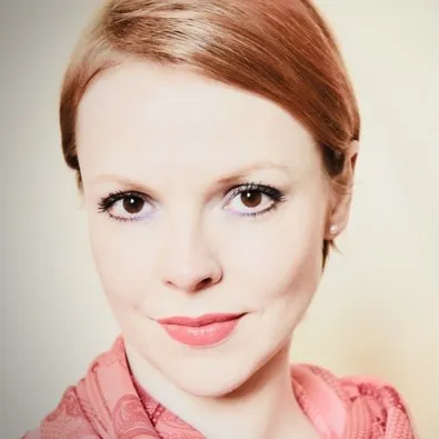 Magdalena, with lightly auburn hair and a pink scarf, against a white background.
