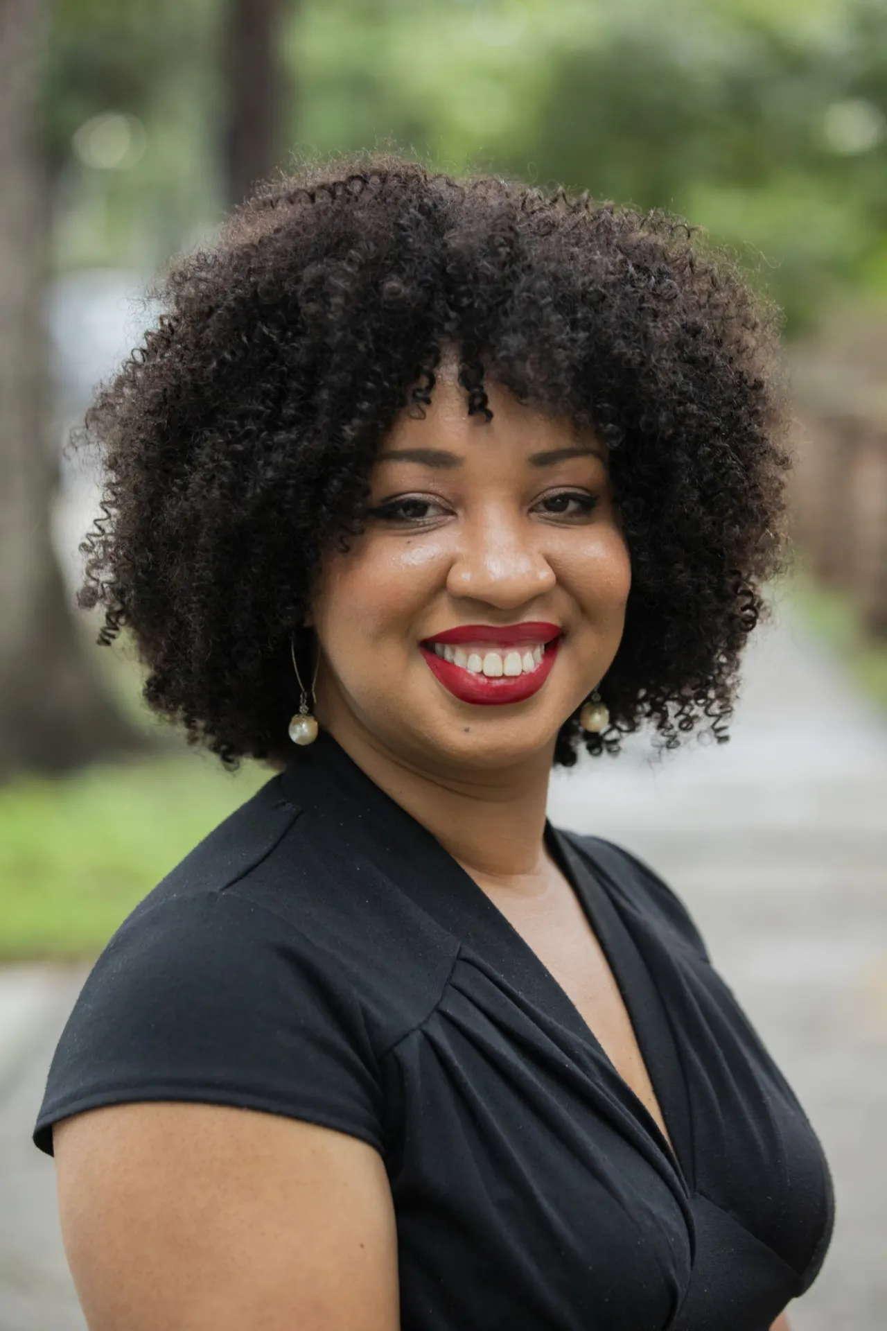 Courtney Bryan smiling at camera in black shirt, with out-of-focus greenery behind.