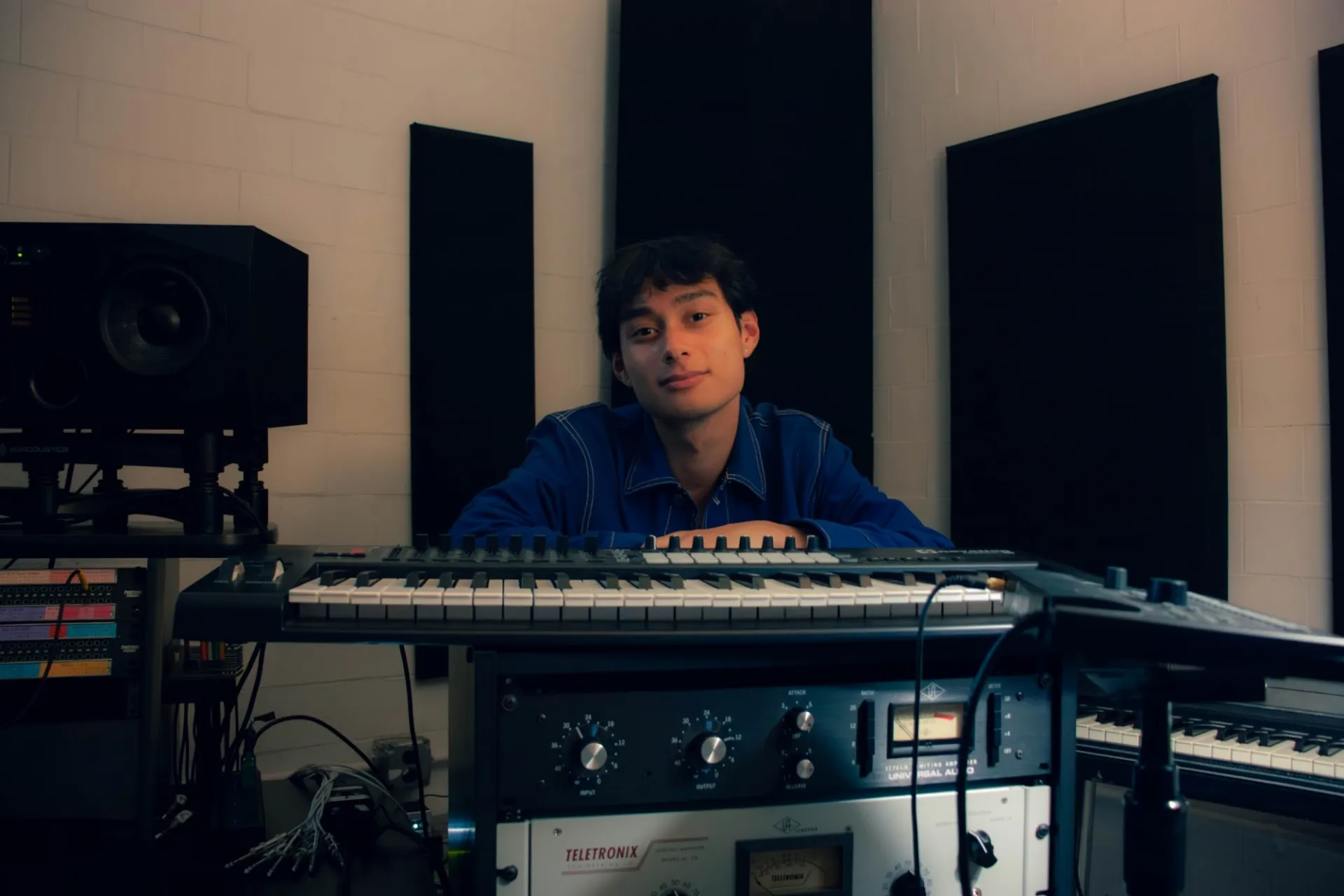 Daniel Weitz sitting in low light in a studio, staring at the camera, keyboard in front of him.