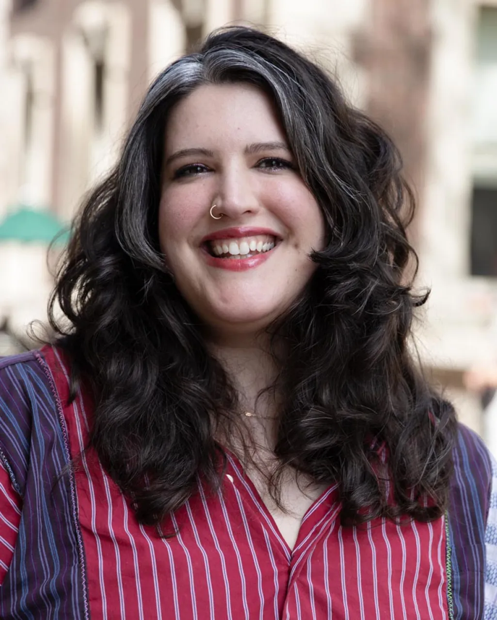 Gabrielle Ferrari smiling outside. She's wearing a blue and red button-down shirt. She has a gray streak running through the front of her hair.