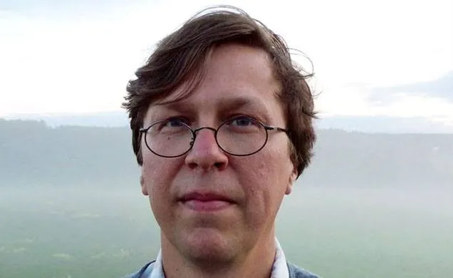 Magnus Granberg in front of a landscape. Just his head is visible, with his glasses and short hair.